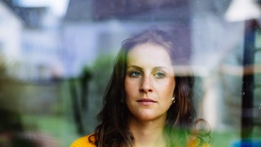 Young woman looks thoughtfully and sadly through the window into the garden with children's toys