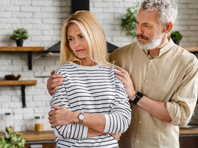 Handsome mature man calming his upset wife while both standing at home