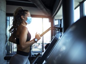 Sportswoman training on treadmill in gym and wearing face mask to protect herself against coronavirus during global pandemic of covid-19 virus.