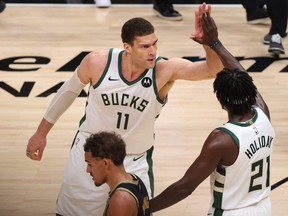 Trae Young, bottom, of the Hawks hangs his head as Brook Lopez, top, and Jrue Holiday, right, of the Bucks celebrate a series win against the Hawks in Game 6 of the NBA's Eastern Conference Finals at State Farm Arena in Atlanta, Saturday, July 3, 2021.