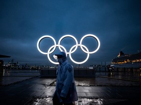 A man walks past the Olympic Rings lit up at dusk in Yokohama on July 2, 2021.