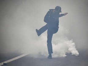 A demonstrator kicks a gas canister to police during clashes at the end of a demonstration part of a national day of protest against French legislation making a Covid-19 health pass compulsory to visit a cafe, board a plane or travel on an inter-city train, in Paris on July 31, 2021.