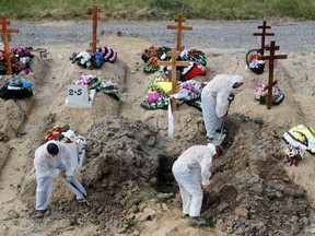 Grave diggers wearing personal protective equipment as a preventive measure against COVID-19 bury a person at a graveyard on the outskirts of Saint Petersburg, Russia, June 25, 2021.