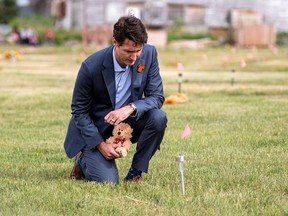 Prime Minister Justin Trudeau lays a teddy bear at a small flag in a field prior to a ceremony at the site of a former residential school, in Cowessess First Nation, Saskatchewan July 6, 2021.