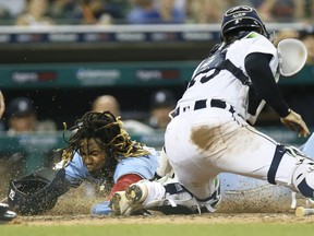 Vladimir Guerrero Jr.  of the Toronto Blue Jays slides past catcher Eric Haase  of the Detroit Tigers to score the go-ahead run during the 10th inning at Comerica Park on August 28, 2021, in Detroit, Michigan.