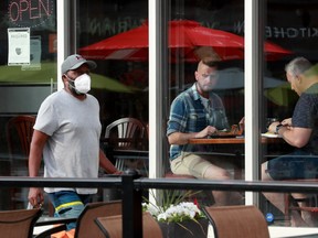 A man in a mask walks past an Ottawa restaurant on July 16, 2021 with maskless indoor diners.