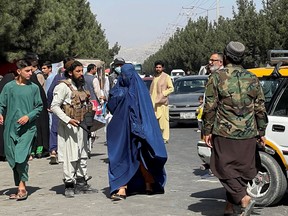 Taliban forces block the roads around the airport, while a woman with Burqa walks passes by, in Kabul, Afghanistan. August 27, 2021.