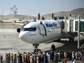 Afghan people climb atop a plane as they wait at the Kabul airport in Kabul on August 16, 2021, after a stunningly swift end to Afghanistan's 20-year war, as thousands of people mobbed the city's airport trying to flee the group's feared hardline brand of Islamist rule.