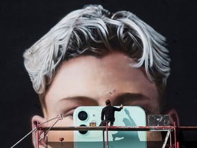 In this file photo taken on Oct. 1, 2020 a graphic artist paints a mural ad for smartphone manufacturer Apple in Berlin.