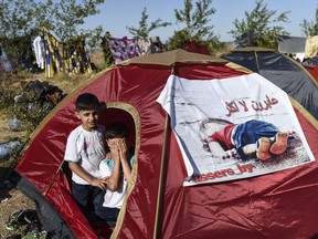 Children sit inside a tent bearing an image of three-year-old Aylan Kurdi, the Syrian toddler who's body washed up on a beach in Turkey,  as Syrian migrants gather near the highway on the way to the Turkish-Bulgarian border at Edirne on September 15, 2015, in Edirne.