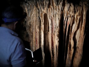 A guide iluminates red ocher markings which were painted on stalagmites by Neanderthals about 65,000 years ago, according to an international study, in a prehistoric cave in Ardales, southern Spain, Aug. 7, 2021.