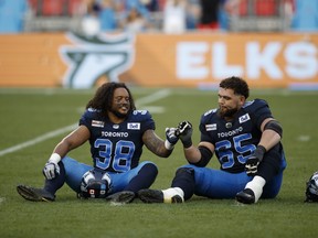 Toronto Argonauts fullback Declan Cross (38) and offensive lineman Dariusz Bladek (65) celebrate their win over the Winnipeg Blue Bombers as a promo for the Argos tilt against the Elks is seen behind them at BMO Field in Toronto, Saturday, Aug. 21, 2021.