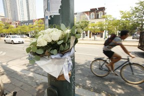 A cyclist pedals past flowers on Monday, Aug. 10, 2021 near where two men were shot to death — and two wounded — on Sunday morning at Spadina Ave. just north of Nassau St. JACK BOLAND/TORONTO SUN