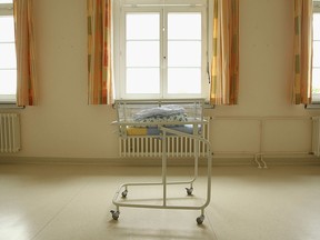 An empty baby bed, which has been placed under a window by the photographer, stands in the maternity ward of a hospital.