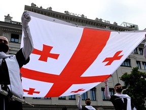 Men wearing national dresses hold the the Georgia's National flag during the celebrations of Georgia's Independence Day in Tbilisi on May 26, 2021.