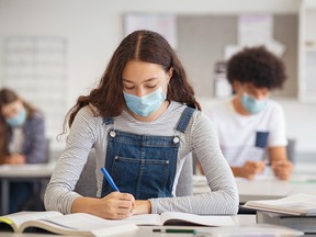 High school students take notes while wearing face masks in the classroom.