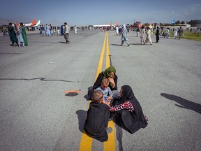 Afghan people sit along the tarmac as they wait to leave the Kabul airport in Kabul on August 16, 2021.