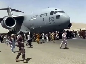 Hundreds of people run alongside a U.S. Air Force C-17 transport plane as it moves down a runway of the international airport, in Kabul, Afghanistan, Monday, Aug.16. 2021.