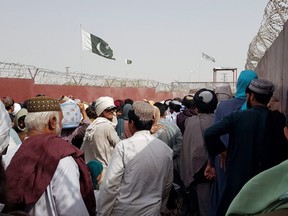 Pakistan's flag and the Taliban's flag are seen in the background as people make their way to Afghanistan at the Friendship Gate crossing point at the Pakistan-Afghanistan border town of Chaman, Pakistan August 15, 2021.