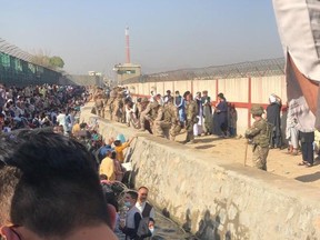 Afghan evacuees, many of whom holding valid Canadian visas and travel documents, stand in an open sewage canal outside of Hamid Karzai International Airport on Tuesday, Aug. 24 2021. Many evacuees told the Toronto Sun that Canadian soldiers on the opposite bank ignored their pleas to look at their paperwork and allow them to board evacuation flights