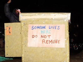 Man showing off his tiny shelter that has a sign on it that reads "Someone lives here, do not remove."