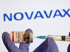 A woman holds a small bottle labeled with a "Coronavirus COVID-19 Vaccine" sticker and a medical syringe in front of displayed Novavax logo in this illustration taken, Oct. 30, 2020.