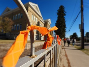 Stanley Jones Elementary School students in Calgary walk past orange ribbons they have tied to a fence outside their school on Wednesday, Sept. 29, 2021 in honour of the first National Day for Truth and Reconciliation. Sept. 30 honours the lost children and survivors of residential schools, their families and communities.
