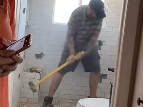 Screenshot of contractor with sledgehammer smashing bathroom tiling.