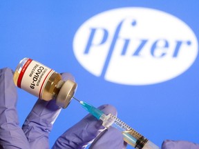 A woman holds a small bottle labeled with a "Coronavirus COVID-19 Vaccine" sticker and a medical syringe in front of displayed Pfizer logo in this illustration taken, Oct. 30, 2020.
