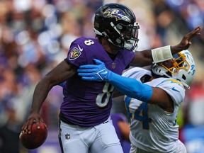 Quarterback Lamar Jackson #8 of the Baltimore Ravens stiff arms outside linebacker Kyzir White #44 of the Los Angeles Chargers during the first half  on October 17, 2021 in Baltimore, Maryland.