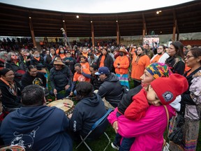 A woman holds a sleeping child as drummers play and people sing during a Tk’emlúps te Secwepemc ceremony to honour residential school survivors and mark the first National Day for Truth and Reconciliation, in Kamloops, BC., on Thursday, September 30, 2021.