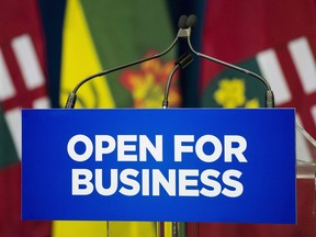 A sign with the slogan "Open for Business" is placed in front of a podium with the Ontario and Saskatchewan flags in the background in Queen's Park in Toronto on October 29, 2018.