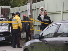 Toronto Police officer Rick Gomez helps Kerry Thomas and George Peters leave flowers at a make-shift memorial for a 36-year-old man known as "Smokey" who was shot to death at an apartment on Eglinton Ave. W., near Keele St., on Saturday, Oct. 23, 2021.