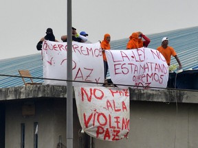 Inmates hold signs while standing atop a roof at the Regional 8 prison, next to the penitentiary, in the outskirts of Guayaquil, Ecuador, on October 2, 2021.