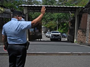 A police officer gestures as vehicles of the Institute of Legal Medicine transport the remains of 12 victims found in a clandestine grave at the home of former police officer Hugo Osorio, in San Salvador, on October 7, 2021. - The general prosecutor's office confirmed that around 30 bodies were found at the home of a police officer in Chalchuapa. (Photo by MARVIN RECINOS / AFP) (Photo by MARVIN RECINOS/AFP via Getty Images)