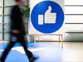 In this file photo taken on Oct. 23, 2019, a Facebook employee walks by a sign displaying the "like" sign at Facebook's corporate headquarters campus in Menlo Park, Calif.