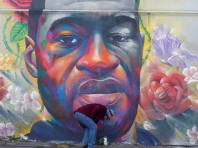 A man places flowers at a mural of George Floyd