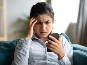 Confused millennial girl sitting at home looking at cellphone