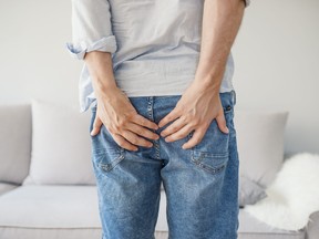 Man holding his bottom in pain, isolated in grey.