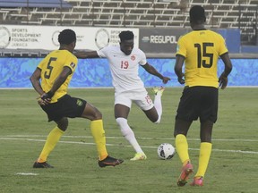 Canada midfielder Alphonso Davies takes a shot against Jamaica's Alvas Powell, left, and Je-vaughn Watson during a qualifying soccer match for the FIFA World Cup Qatar 2022 at the Independence Park stadium in Kingston, Jamaica, Sunday, Oct. 10, 2021.