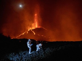 In this handout photograph taken and released by the Spanish Military Emergency Unit (UME) on October 16, 2021, members of the GIETMA (Technological and Environmental Emergencies Intervention Group) of the UME monitor the evolution of a new lava flow, following the eruption of the Cumbre Vieja volcano, on the Canary island of La Palma.