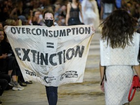 A demonstrator holds a banner as models walk the runway during the Louis Vuitton Womenswear Spring/Summer 2022 show as part of Paris Fashion Week on Oct. 5, 2021 in Paris.