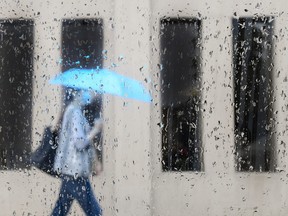 A pedestrian walks alongside businesses on a rainy day while wearing a protective mask during the COVID-19 pandemic in Toronto on Friday, June 18, 2021.
