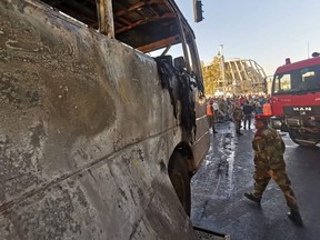 Syrian security forces stand guard as the charred bus is removed from the site of an early morning attack on an army bus targeted with explosive devices, in the capital Damascus on October 20, 2021.