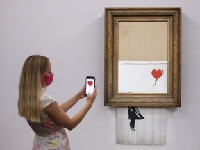 A gallery assistant poses by 'Love is in the Bin', an artwork by Banksy, which will be for sale in an auction, at Sotheby's in London, Britain, September 3, 2021.