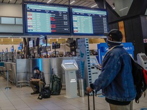 A passenger holds his mobile phone while looking at an electronic flight notice board displaying cancelled flights at OR Tambo International Airport in Johannesburg on Nov. 27, 2021, after several countries banned flights from South Africa following the discovery of a new COVID-19 variant Omicron.
