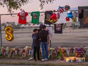 In this file photo taken on November 7, Isaac Hernandez and Matthias Coronel watch Jesus Martinez sign a remembrance board at a makeshift memorial at the NRG Park grounds where eight people died in a crowd surge at the Astroworld Festival in Houston, Texas.
