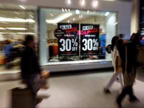 Shoppers walk by advertisements at a retail store during Black Friday sales at Roosevelt Field shopping mall in Garden City, New York, Nov. 26, 2021.