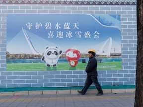 A worker walks past a poster showing the mascots of the Beijing 2022 Olympic and Paralympic Winter Games in Beijing, China, Tuesday, Nov. 30, 2021.