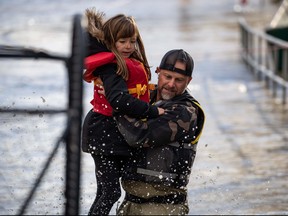 A volunteer carries a young girl to high ground after using a boat to rescue a stranded woman and children stranded near Abbotsford on Tuesday. (THE CANADIAN PRESS/Darryl Dyck)
